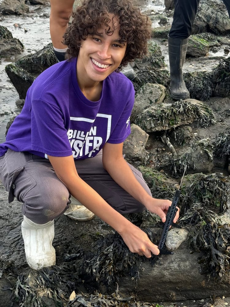 Young volunteer kneels on rocks during a shoreline activity