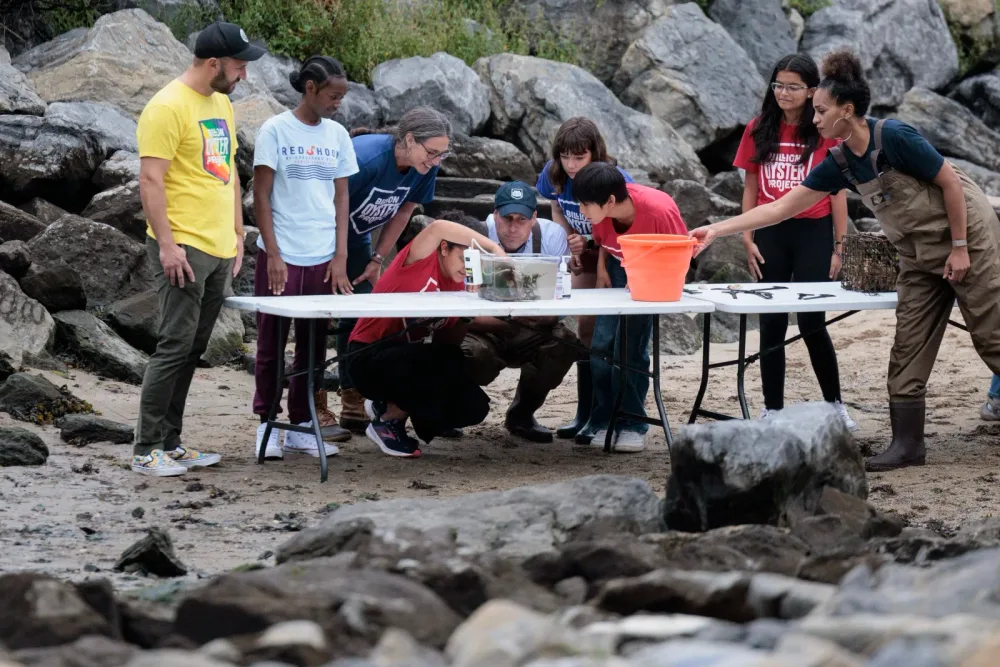 Prince William and students gather around a waterfront activity table