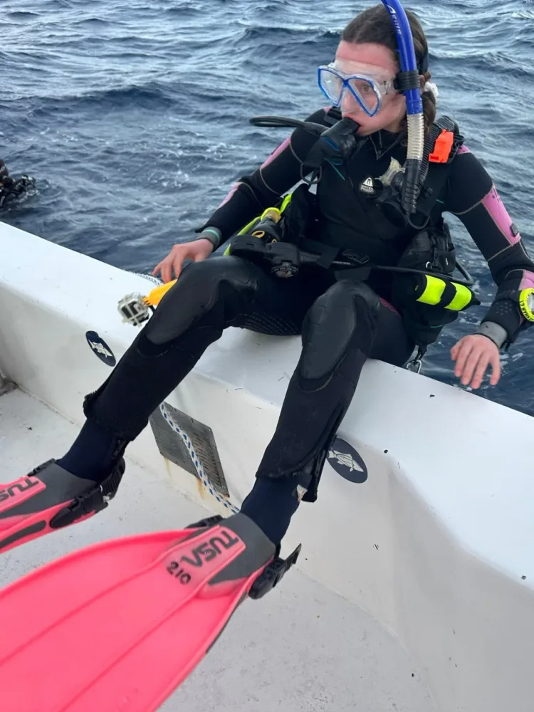 Scuba diver sits on the side of a boat wearing fins