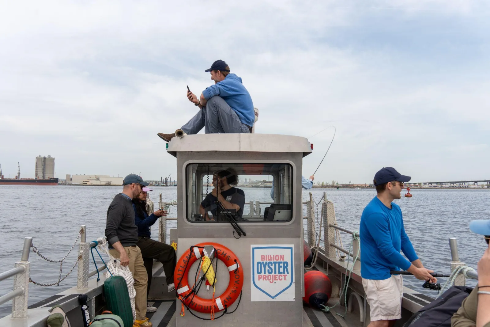 People aboard a Billion Oyster Project boat on New York Harbor with the industrial waterfront behind them