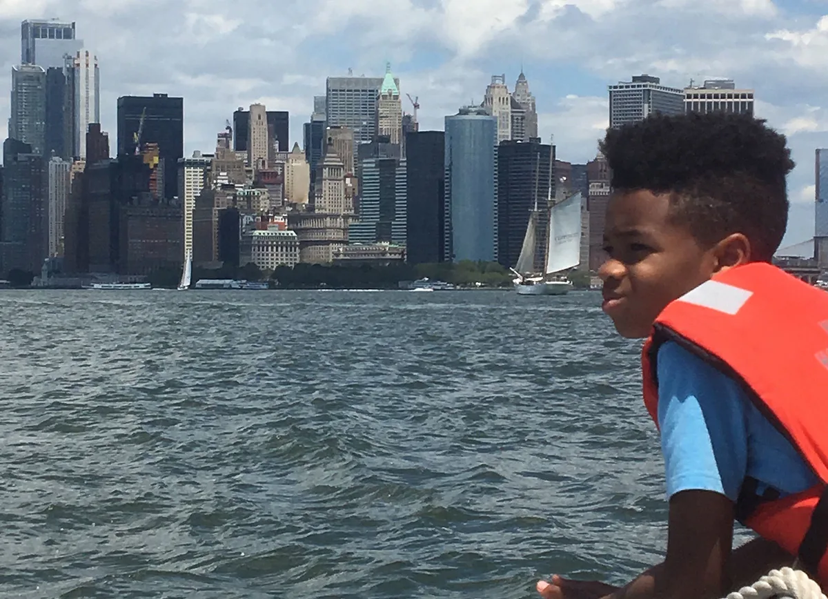 A student in a life jacket looks across New York Harbor toward Lower Manhattan