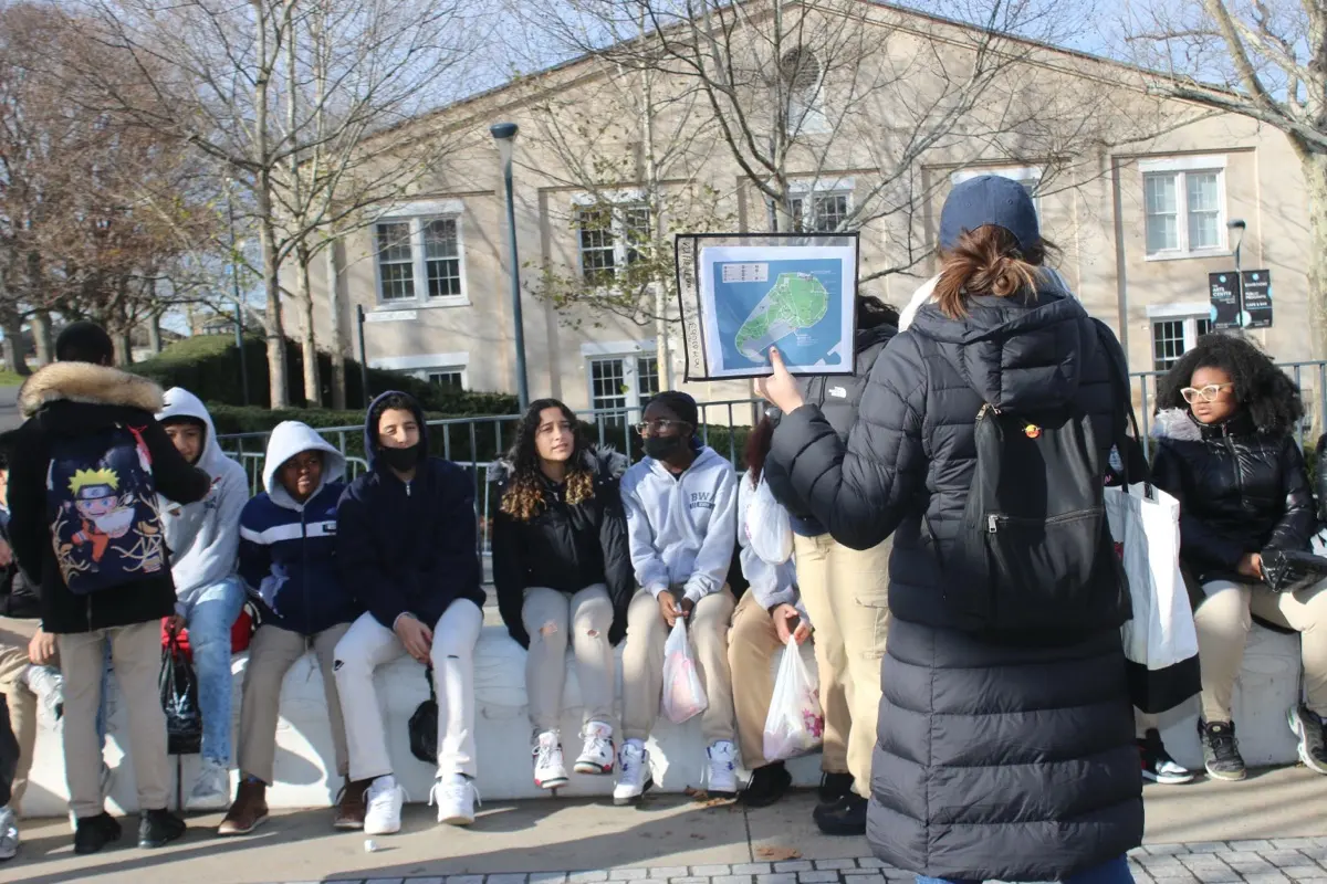 A guide holds a map of Governors Island while students gather outside New York Harbor School