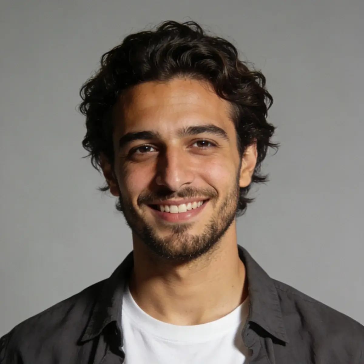 Portrait of a man with short dark hair and a light beard wearing casual attire against a neutral background