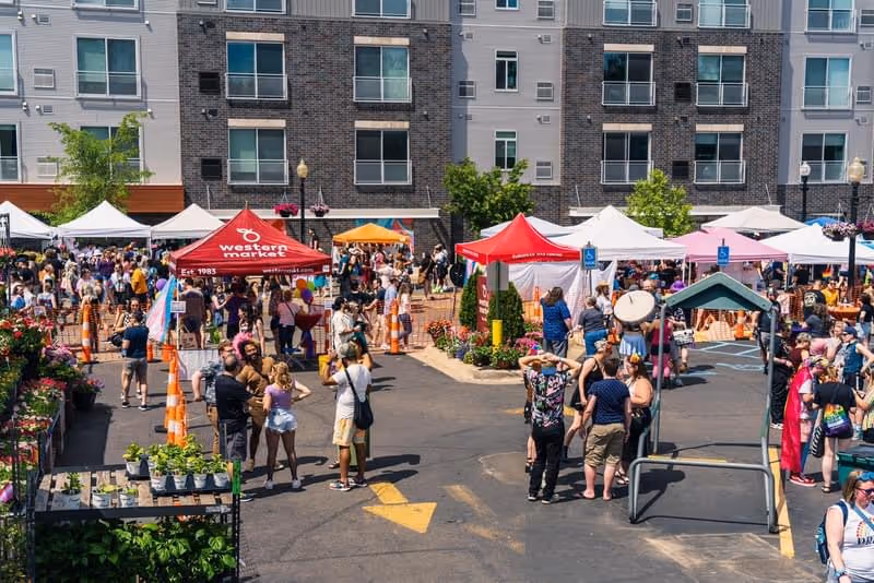 A wide view of the event shows multiple vendor tents, plants for sale, and a bustling crowd enjoying Western Market’s Pride celebration.