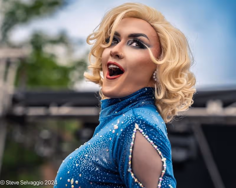A drag performer in a sparkling blue outfit poses and smiles during the Pride celebration at Western Market.