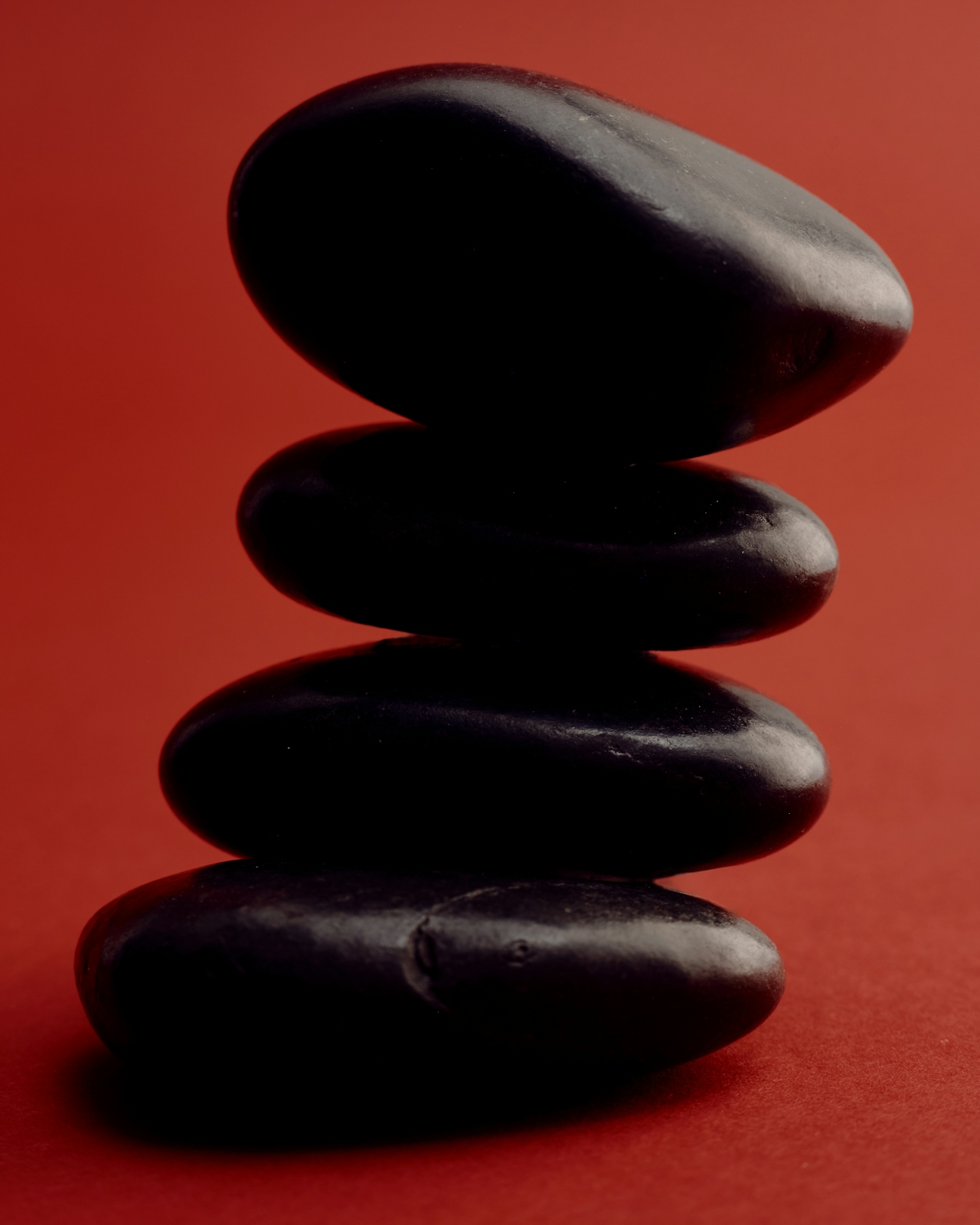 Stack of four smooth black stones balanced on a red background.