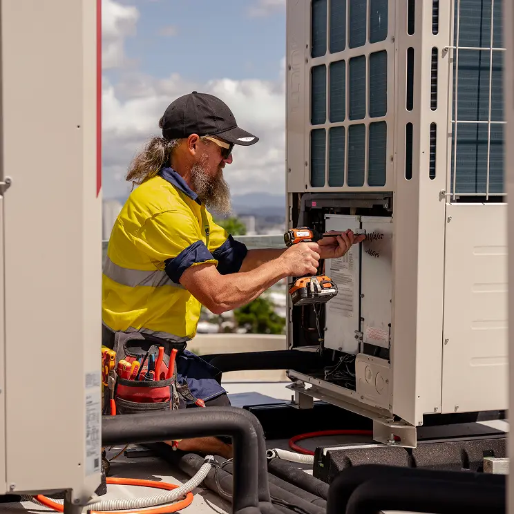 HVAC technician repairing a rooftop air conditioning unit with a power drill.