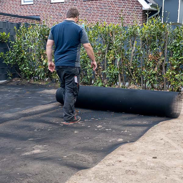 Ein Mann in Arbeitskleidung rollt eine Rolle Maulwurfsgitter auf den vorbereiteten Boden