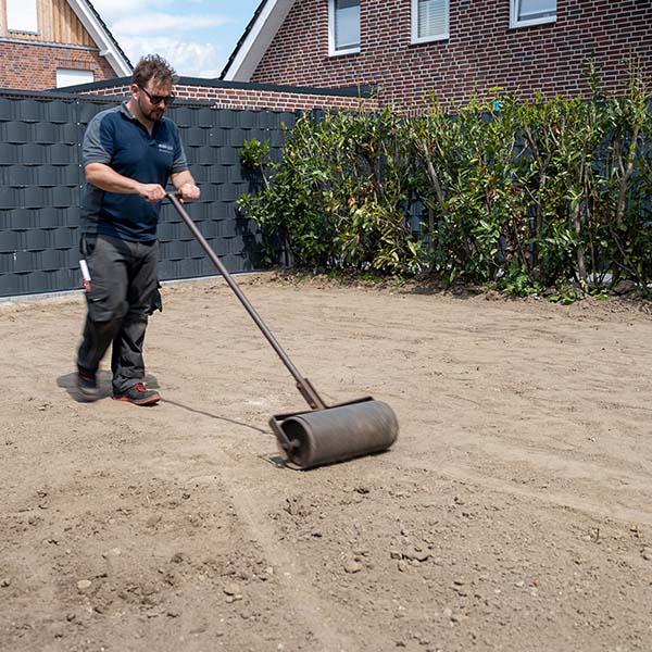 Eine Mann in Arbeitskleidung beendet den Mutterboden mit einer Walze
