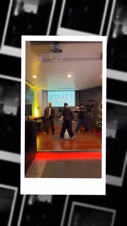 Three people dancing in a room with wooden floor, projector screen displaying 'GIAU,' and a decorated Christmas tree.