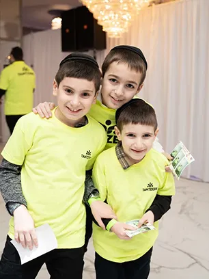 Three smiling boys wearing yellow Tantzter shirts at an indoor event, two holding flyers.