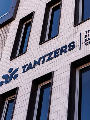 Facade of a modern building with large black-framed windows and the text 'TANTZERS' mounted on light-colored tile walls.