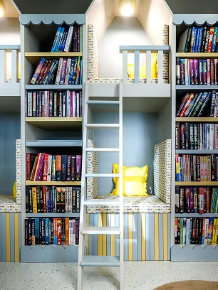 Cozy reading nook with a ladder, surrounded by shelves filled with colorful books and featuring cushioned seating areas with yellow pillows.