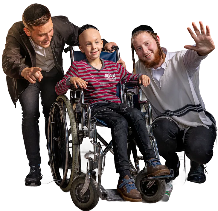 Two young men with kippahs smiling and supporting a boy in a wheelchair, who is also smiling and wearing a red striped shirt.
