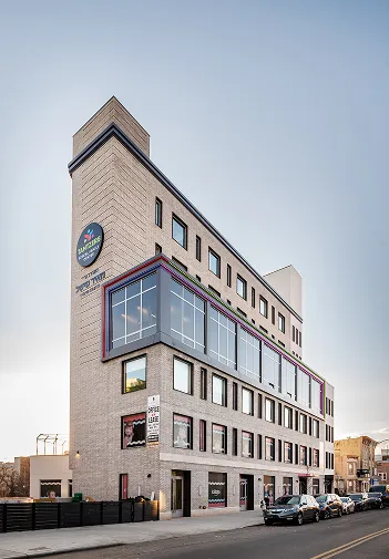Modern multi-story brick building with large windows and parked cars on the street in front.