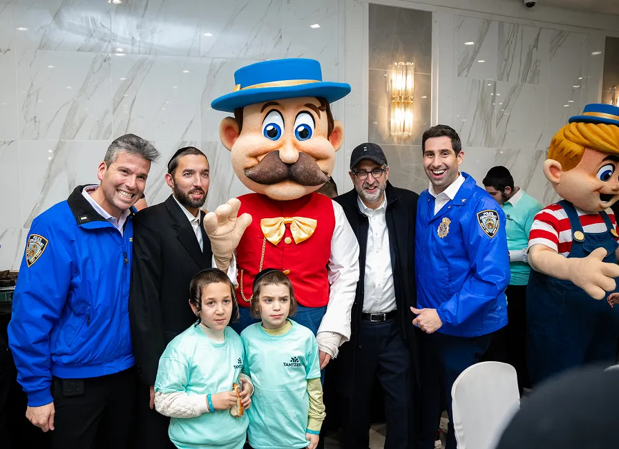 Group photo of adults and children with two mascots in a brightly lit room with marble walls.