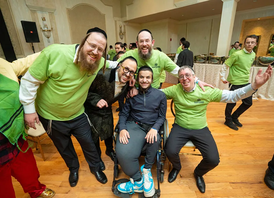Group of smiling men, one in a wheelchair, posing together in a social event setting.