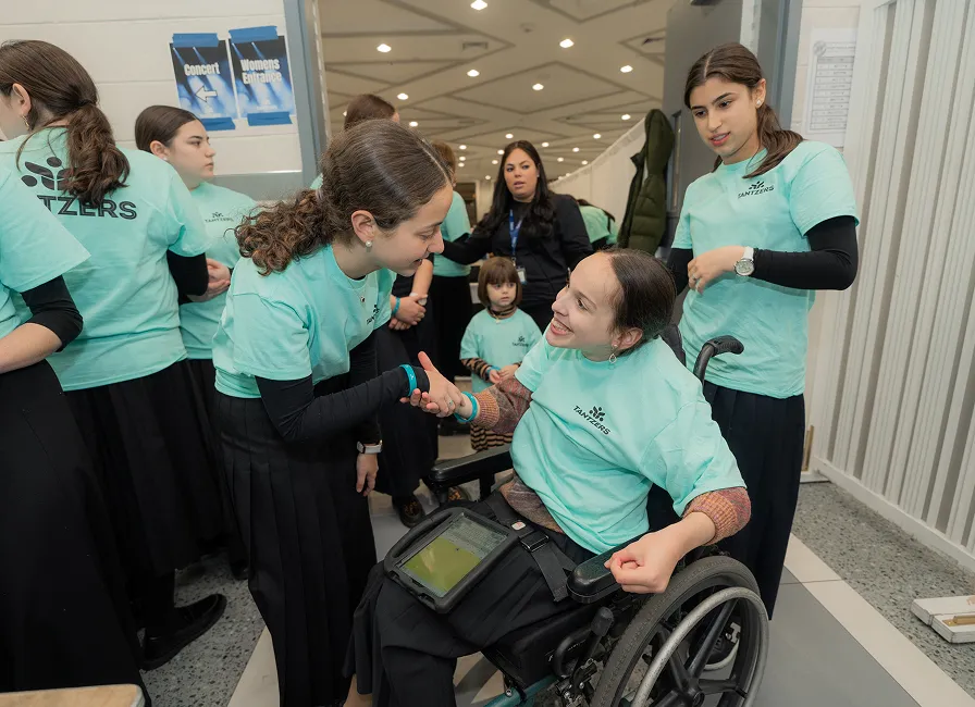 Group of young women wearing light blue shirts, one in a wheelchair smiling and shaking hands.