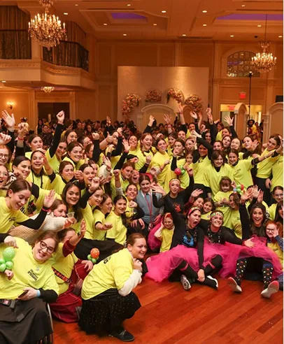 Large group of people in yellow shirts smiling and posing joyfully in a decorated indoor event space.