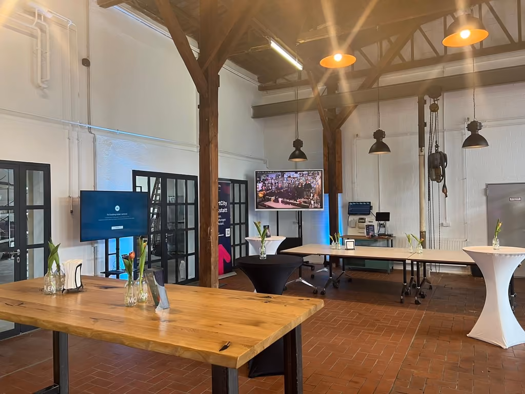 Vielseitiger Workshop- und Eventbereich der SmartCityWerkstatt mit Holztischen, Stehtischen und moderner Präsentationstechnik