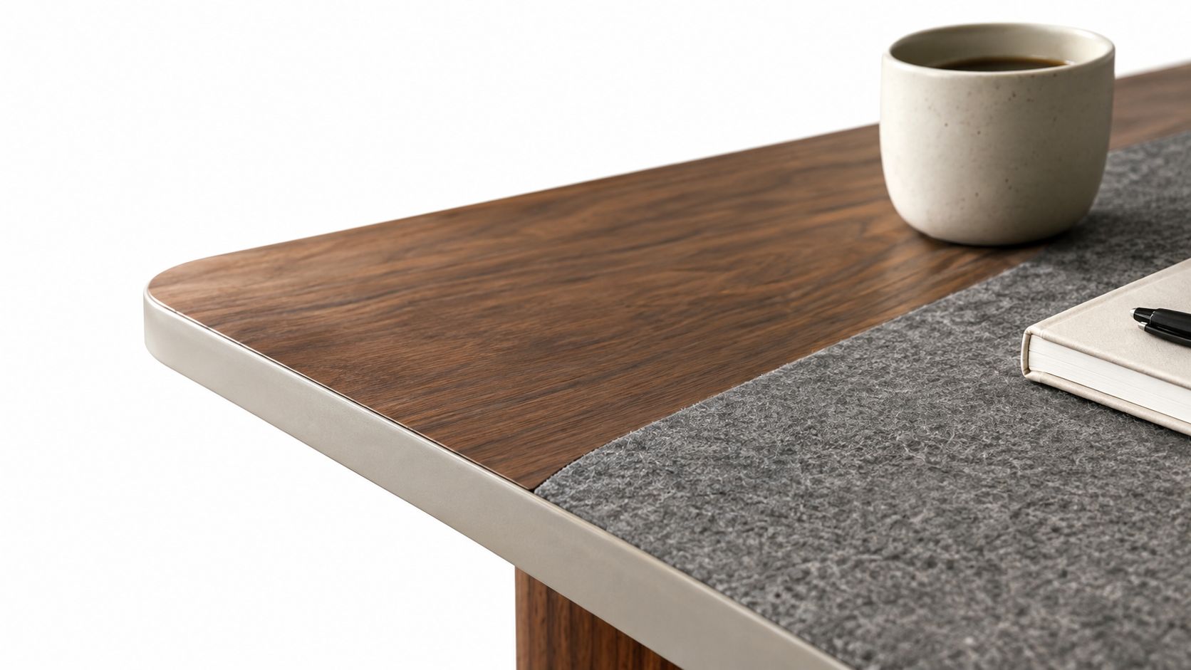 Eine Nahaufnahme einer modernen Schreibtischplatte aus dunklem Holz mit einer grauen Filzunterlage, einer Kaffeetasse und einem Notizbuch.
