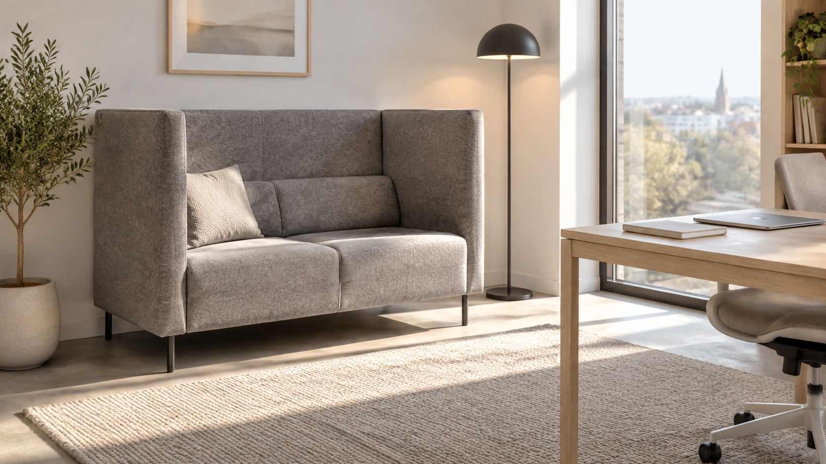 Ein gemütliches graues Akustik-Sofa in einem hellen, modern eingerichteten Büro mit einem Fenster und einem Schreibtisch.