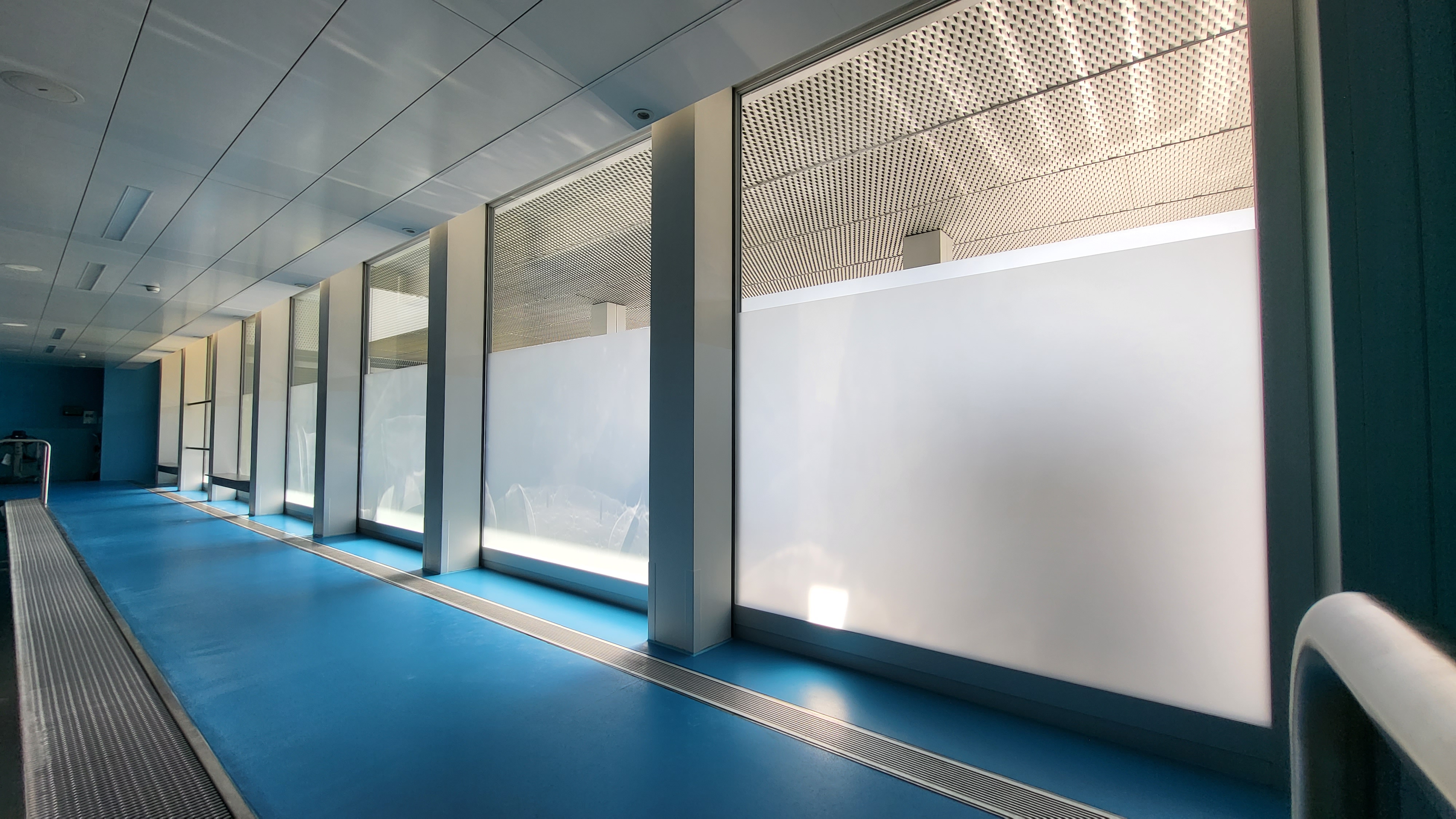 Ein modernes Gebäude mit braunen Fassadenelementen und großen Fenstern; darunter stehen zwei Personen freudig auf einem glänzenden Solarpaneldach unter klarem blauem Himmel.