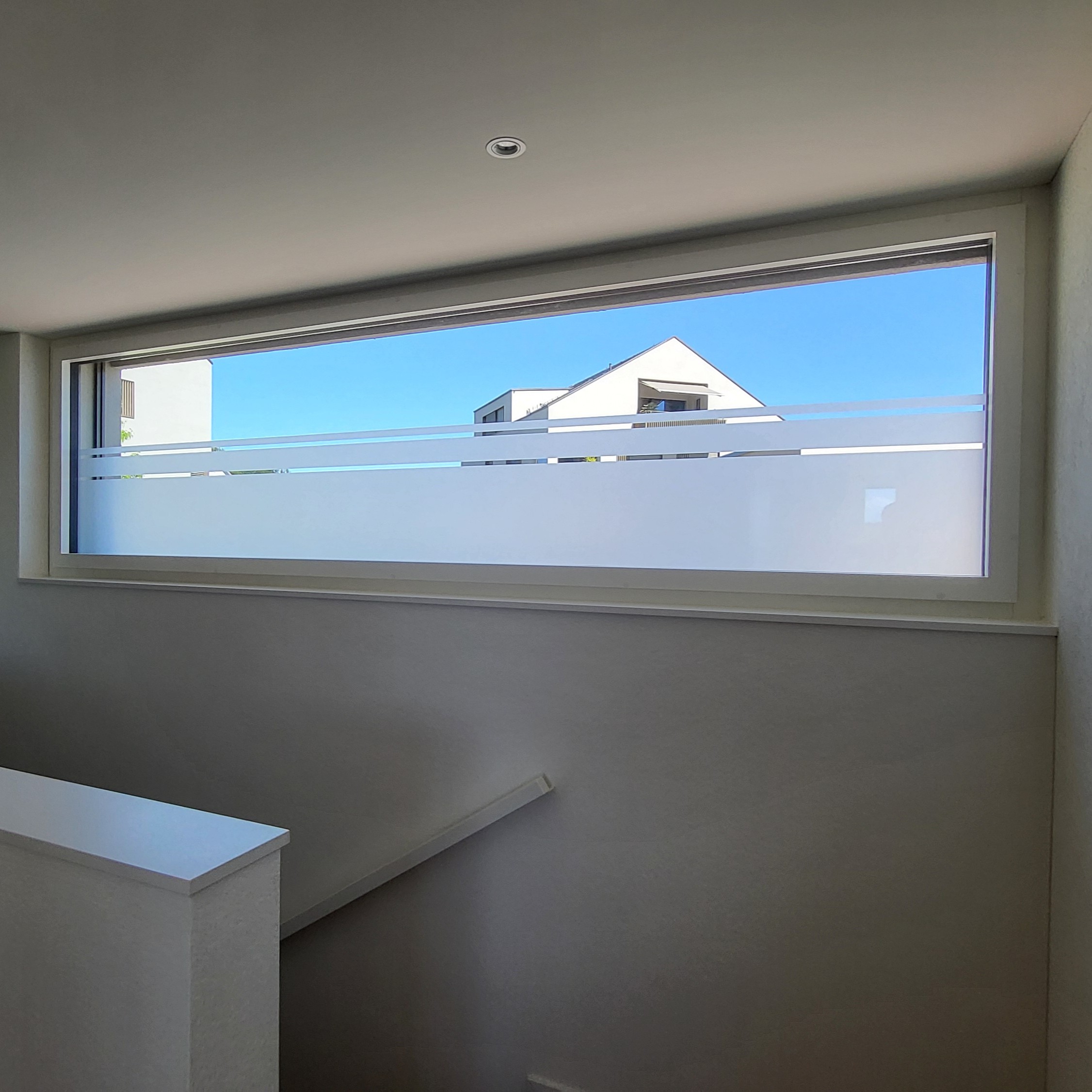 Fenster mit blick auf weiße moderne Gebäude bei blauem Himmel von innen über Treppe.