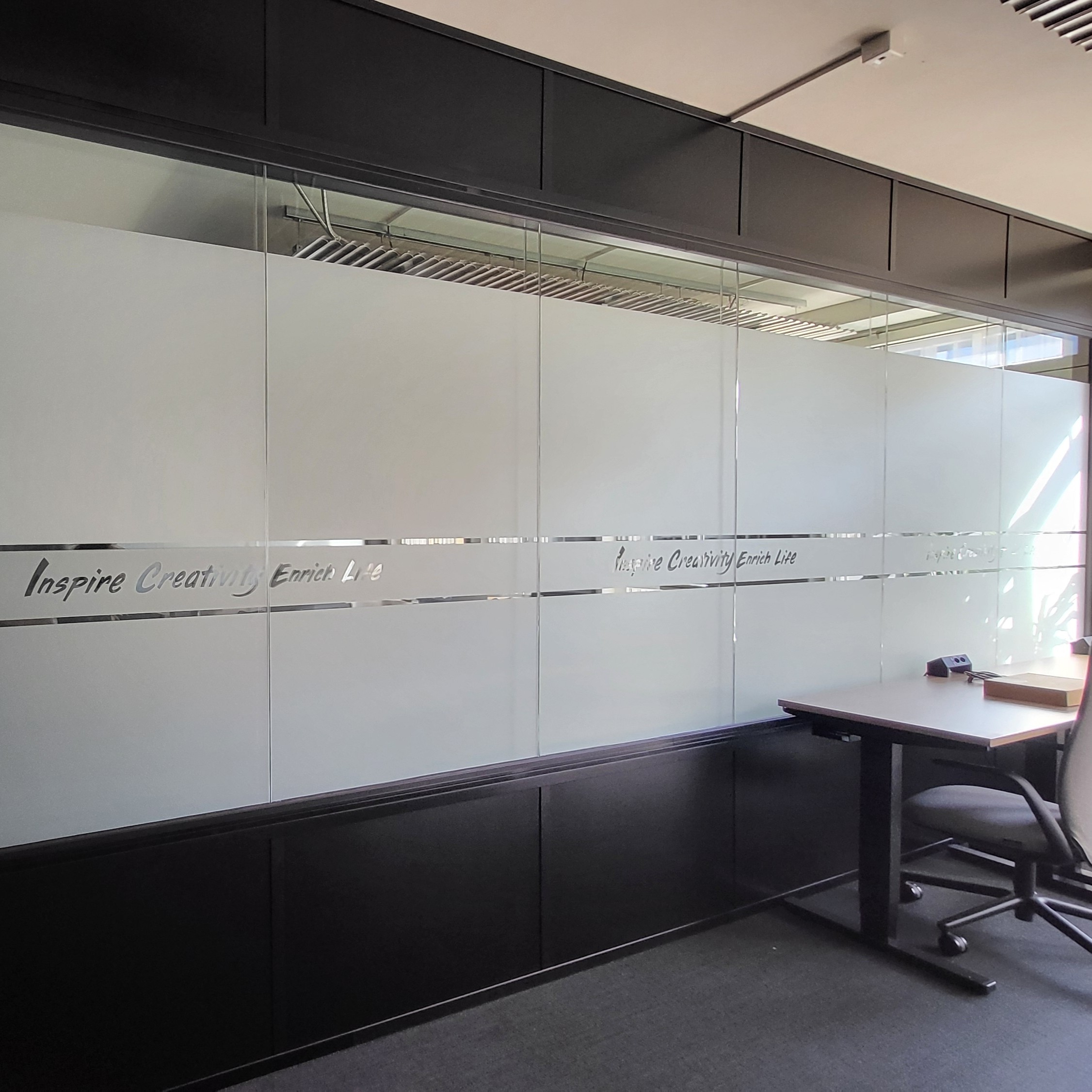 Modern office corner with frosted glass panel showing 'Inspire Creativity Enrich Life' text strip.