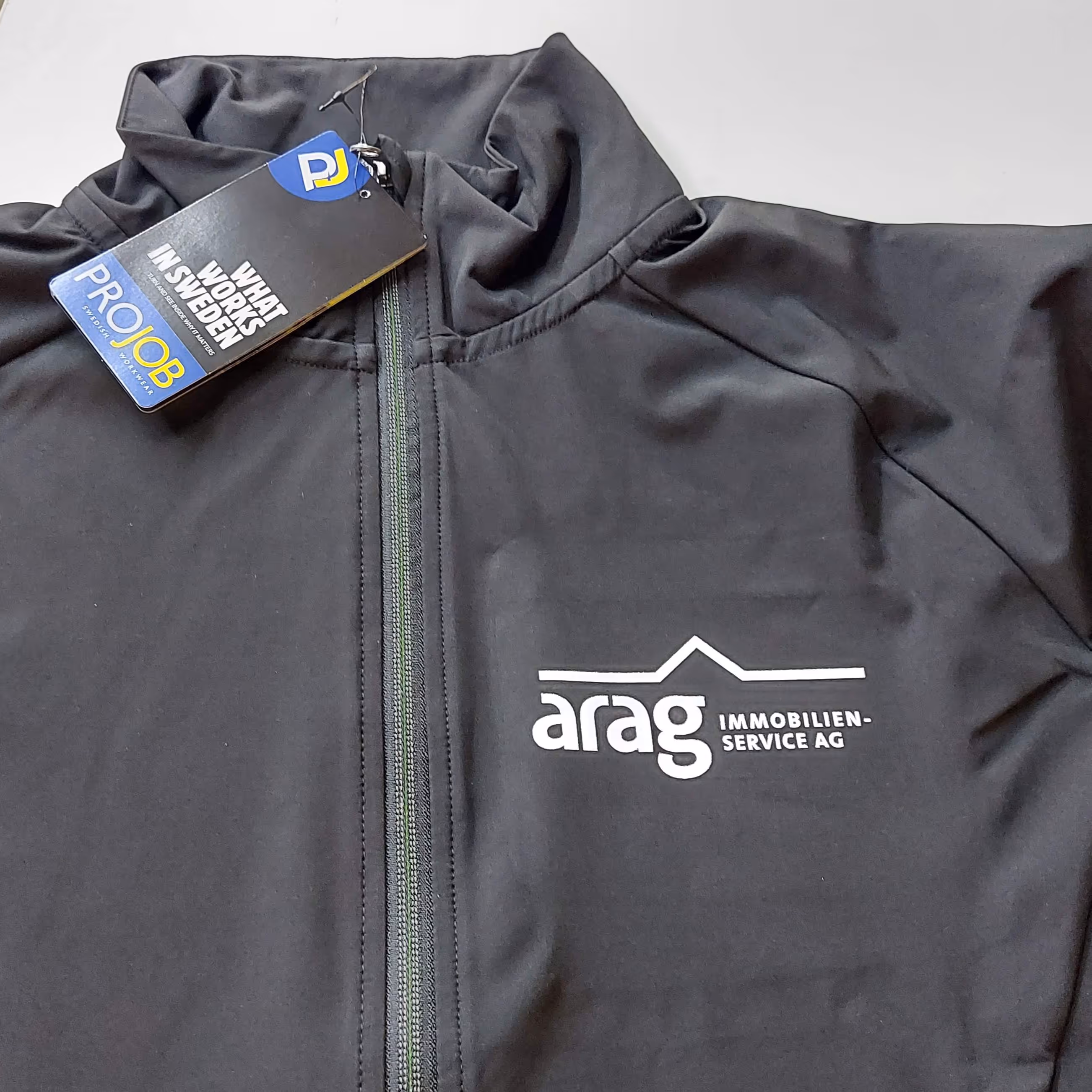 Schwarze Jacke mit Reissverschluss und Aufdruck 'arag Immobilien-Service AG' und ProJob Etikett.