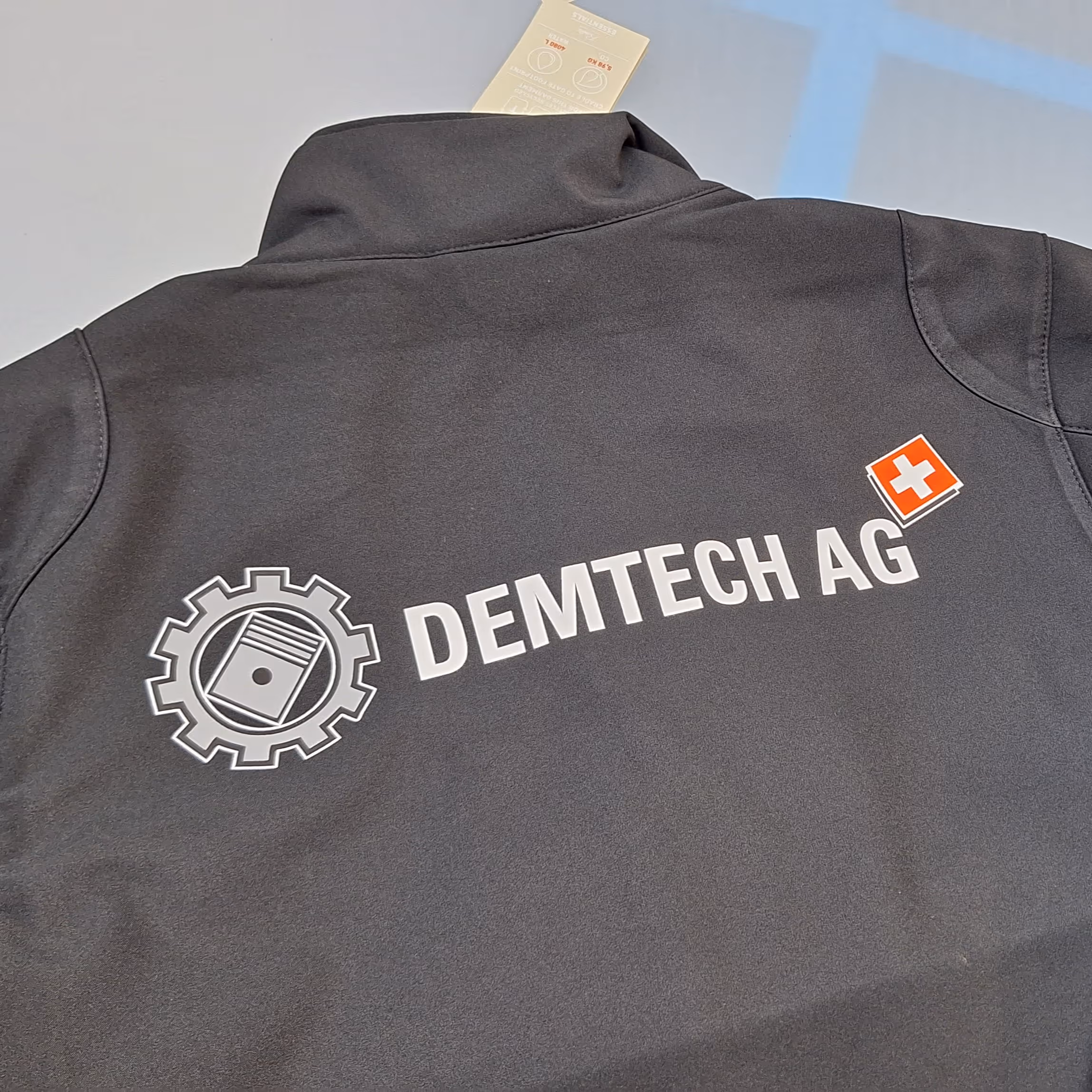 Schwarze Jacke mit Logo und Schriftzug DEMTECH AG sowie Schweizer Flagge auf dem Rücken.