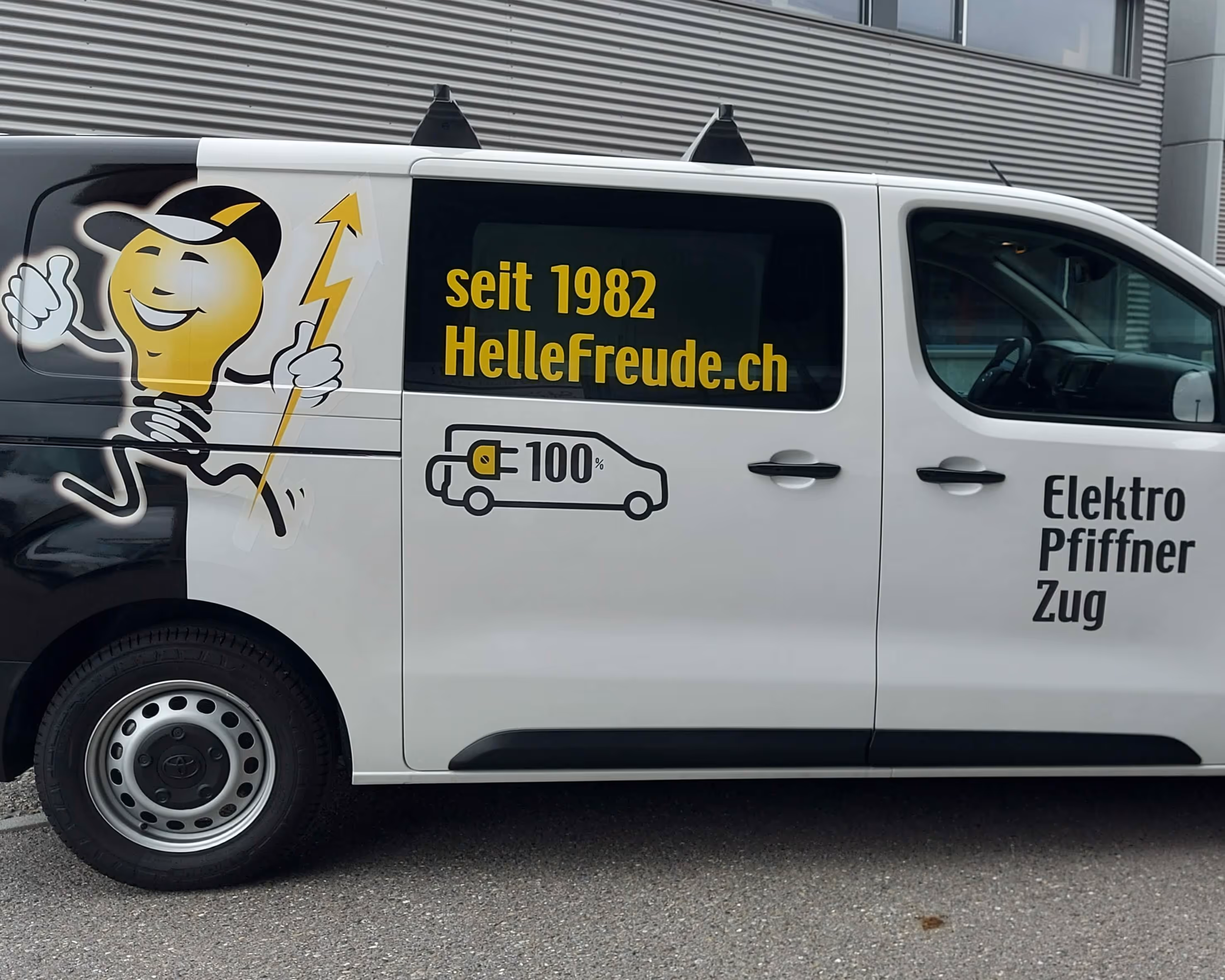 Weisser Elektrotransporter mit gelbem Glühbirnenmaskottchen und Text von Elektro Pfiffner Zug