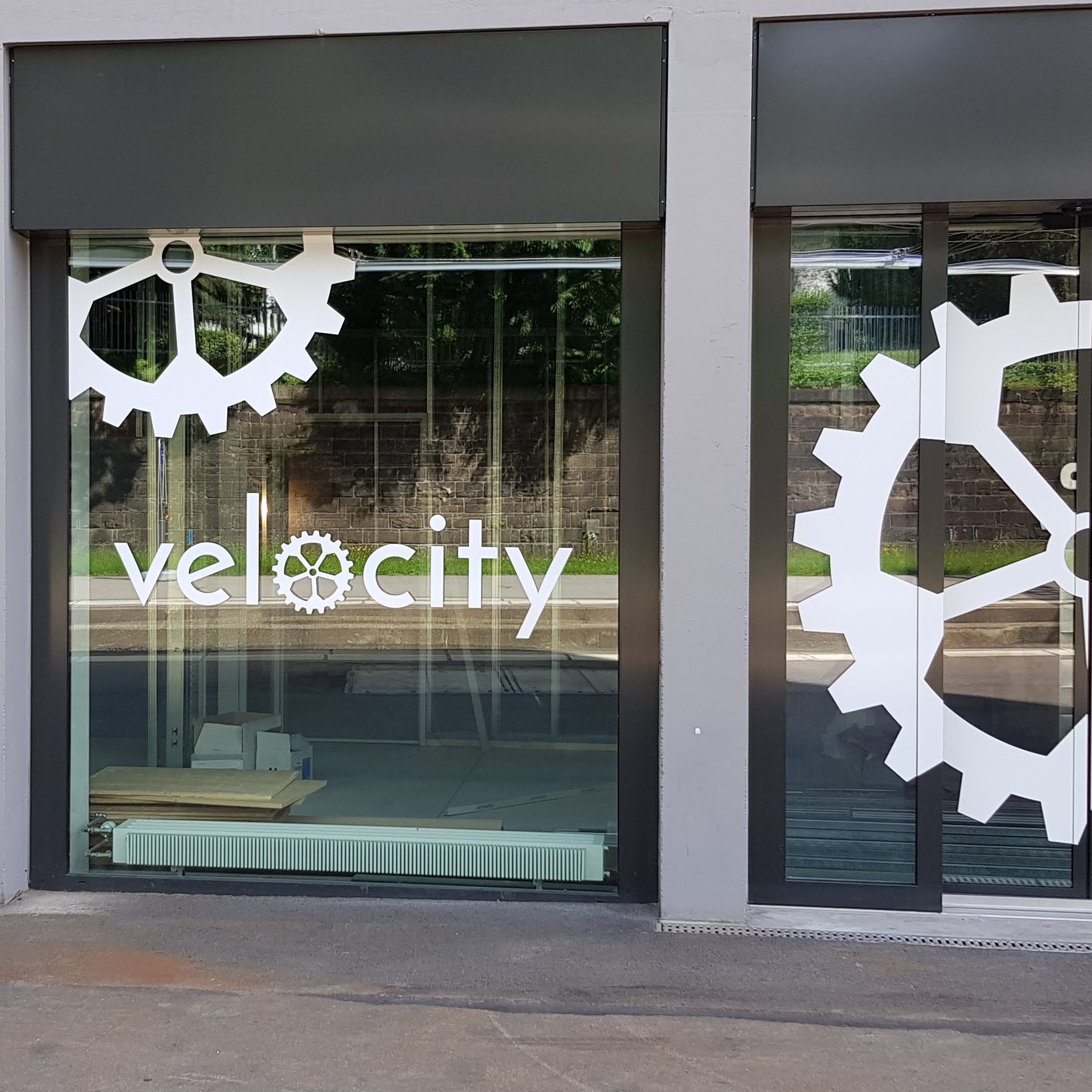 Fensterfront mit dem Schriftzug "velocity" und Zahnradsymbolen auf Glasflächen eines Gebäudes.