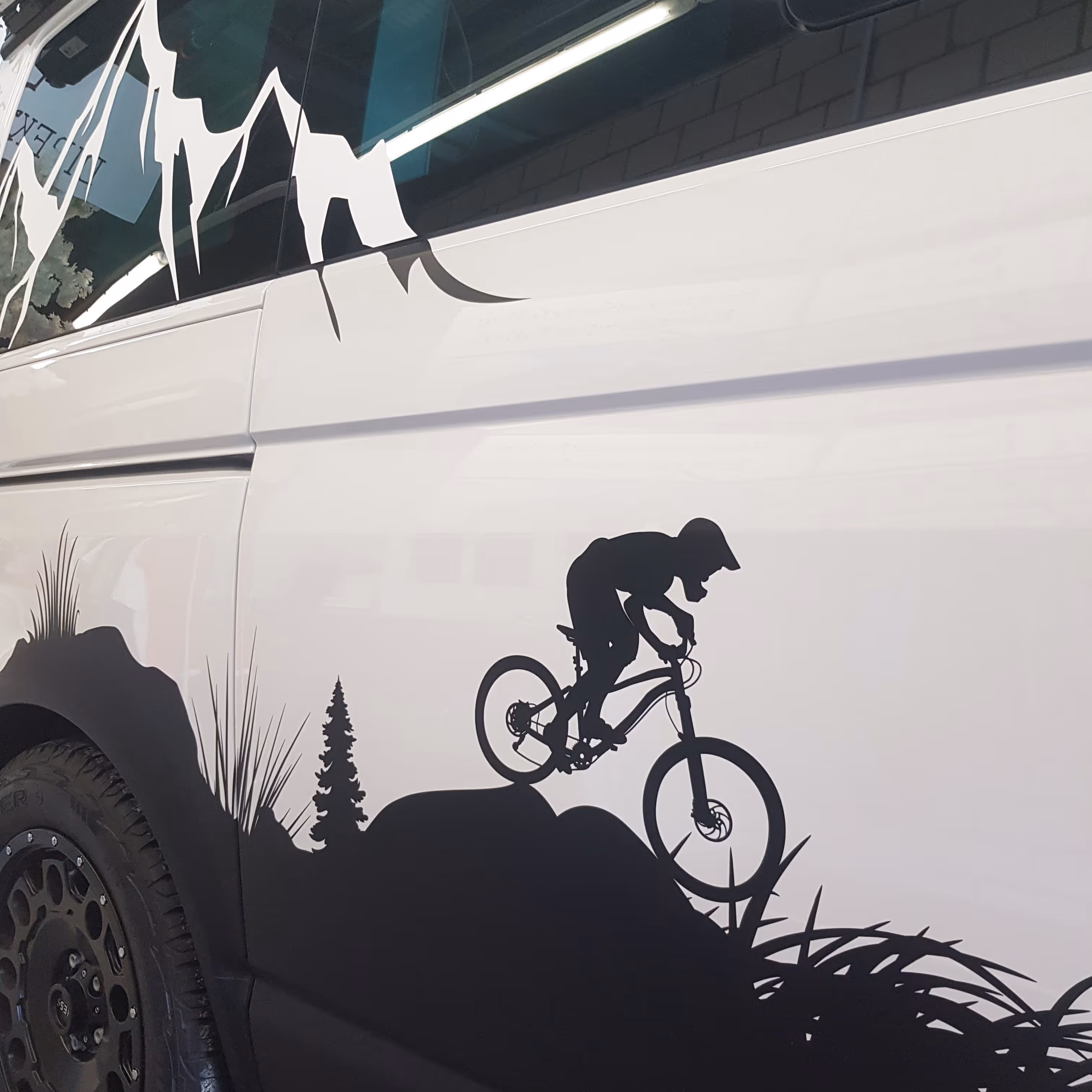 Schwarzweiße Grafik eines Mountainbikers, der auf einem Felsabhang entlangfährt, auf einem weissen Fahrzeug.