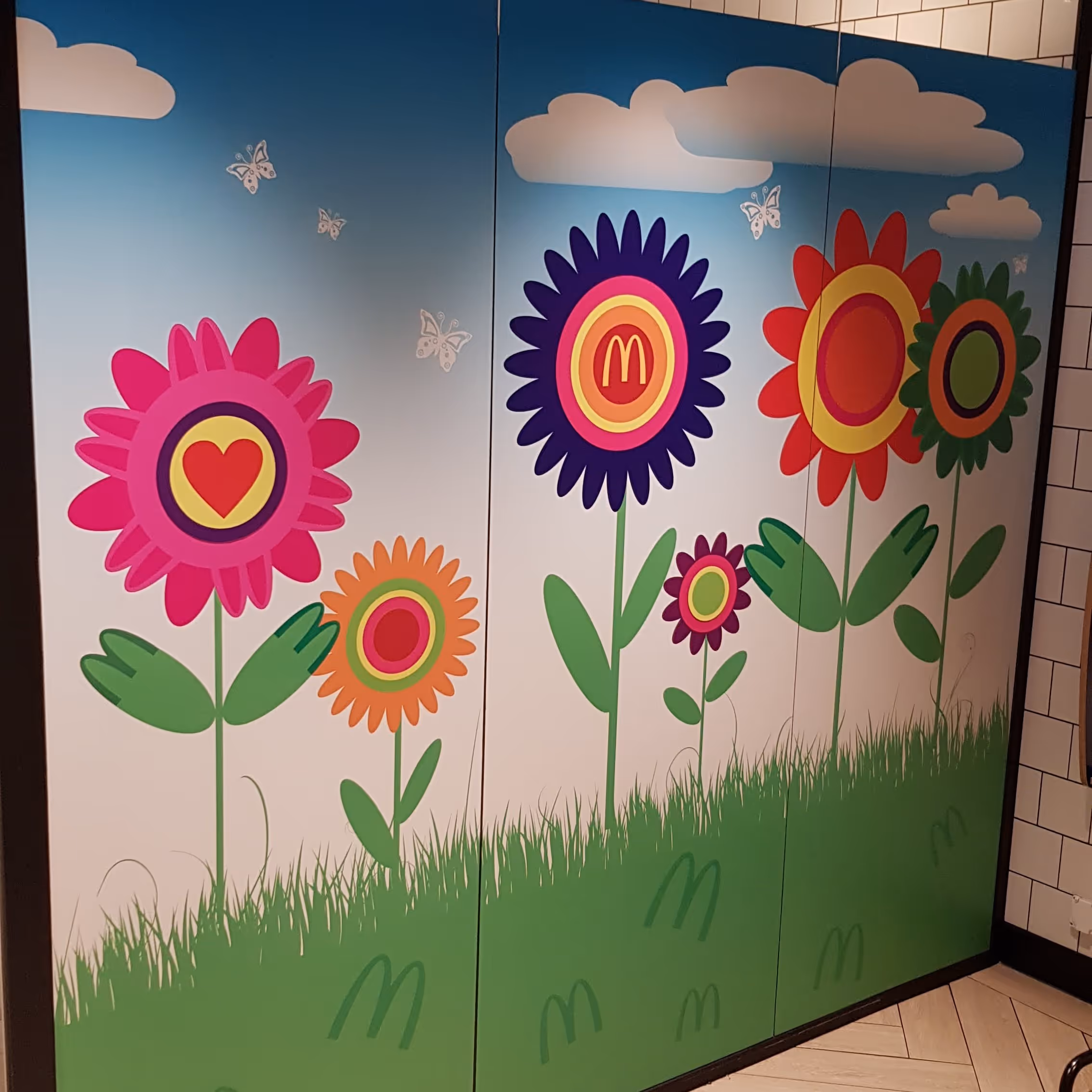 Bunte Blumenillustrationen mit Herzen, Schmetterlingen und McDonald's-Logos auf einer Wand.