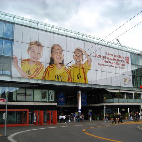 Großes Banner mit drei Kindern in gelben McDonald's Trikots an einem modernen Gebäude in Bern.