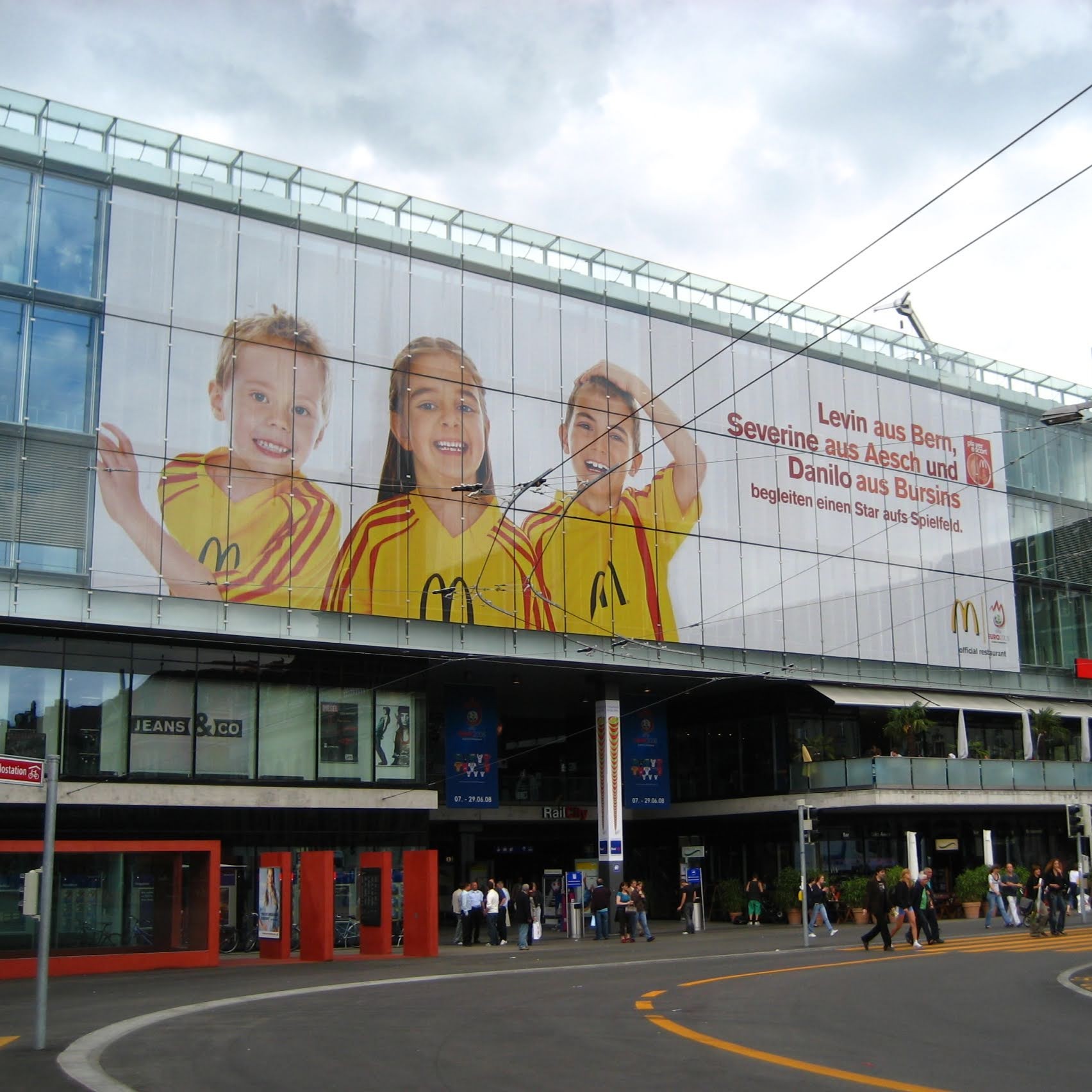 Großes Banner mit drei Kindern in gelben McDonald's Trikots an einem modernen Gebäude in Bern.