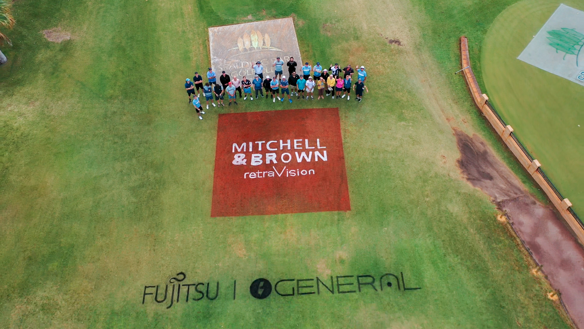 Aerial view of Mitchell & Brown sponsor logo on a golf course with group of players
