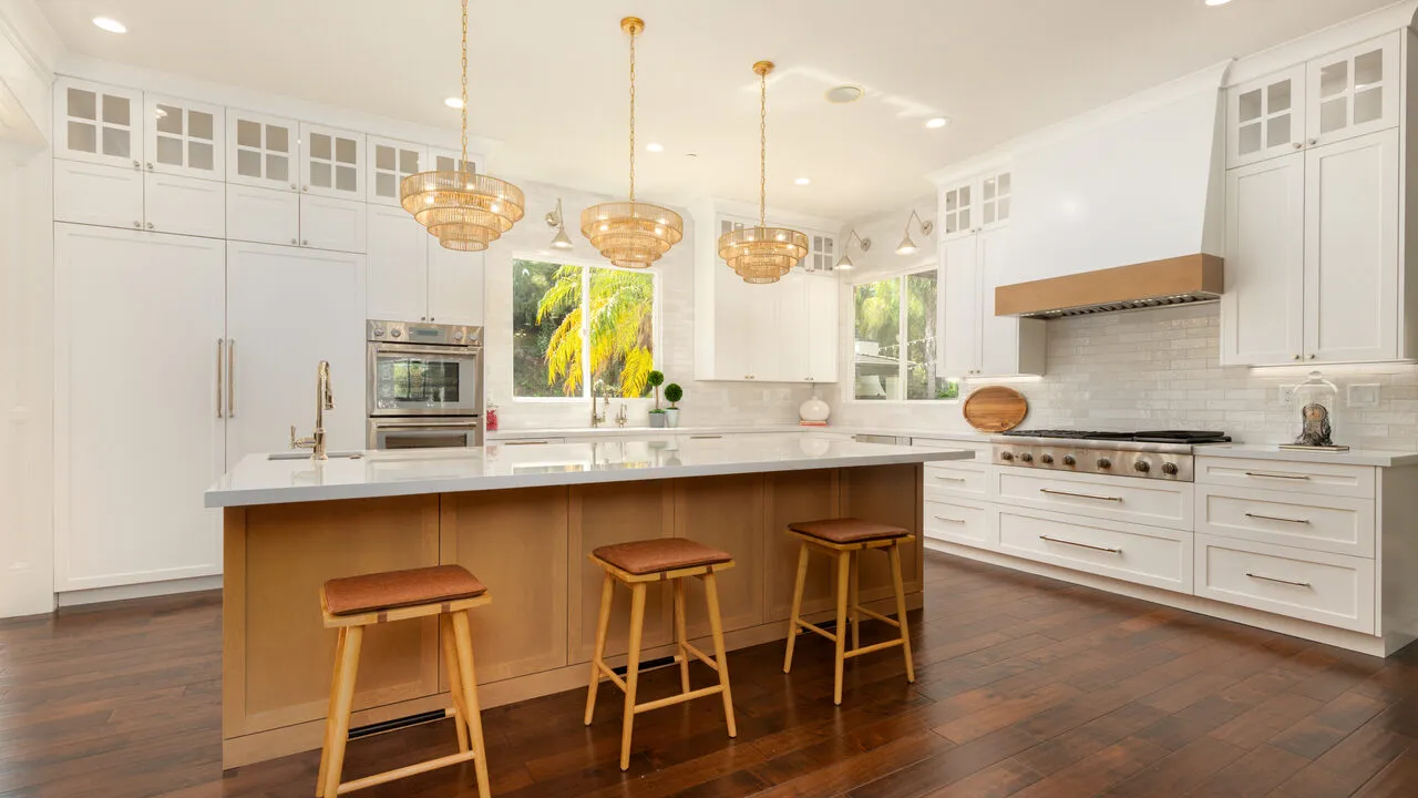 Bright modern kitchen with white cabinetry, large island with three wooden stools, hardwood floors, and three pendant lights.