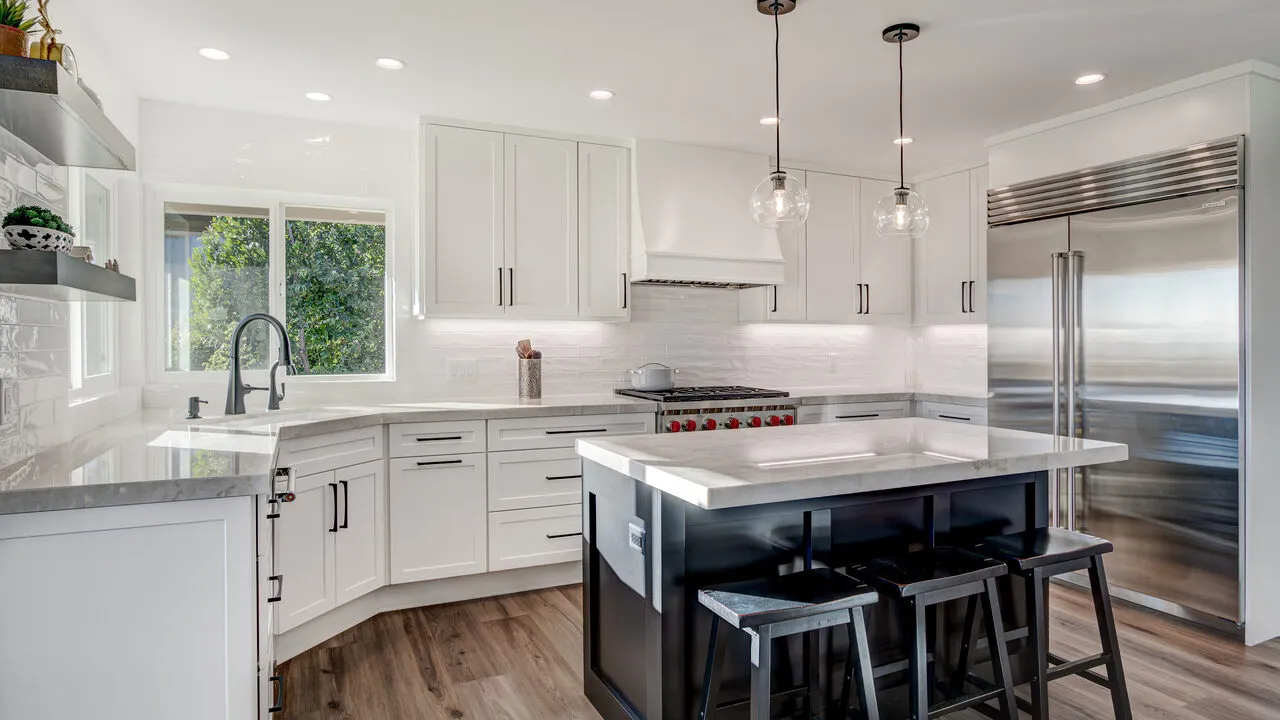 Modern kitchen with white cabinets, marble countertops, a large stainless steel refrigerator, and a black island with three stools.