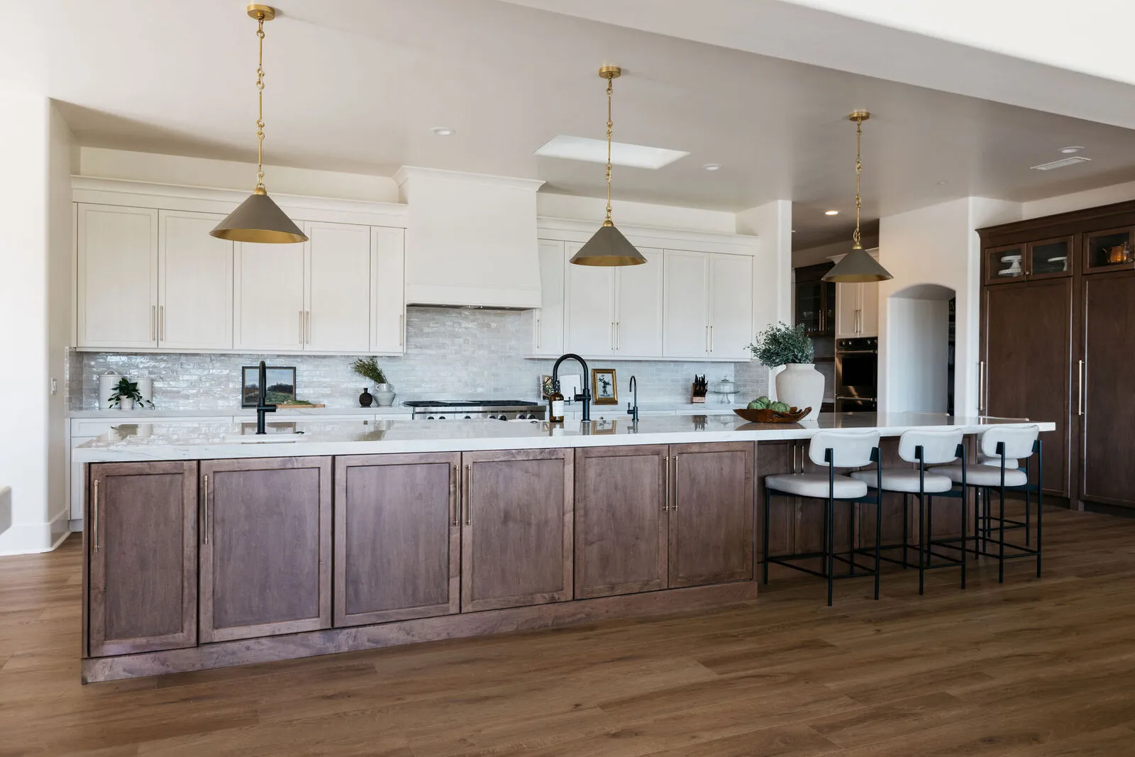 Modern kitchen with white upper cabinets, brown lower cabinets, marble countertop island with three chairs, and three pendant lights.