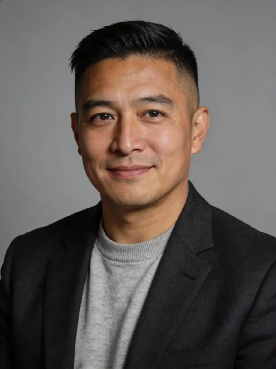 Portrait of a man with short black hair wearing a gray sweater and black blazer against a gray background.