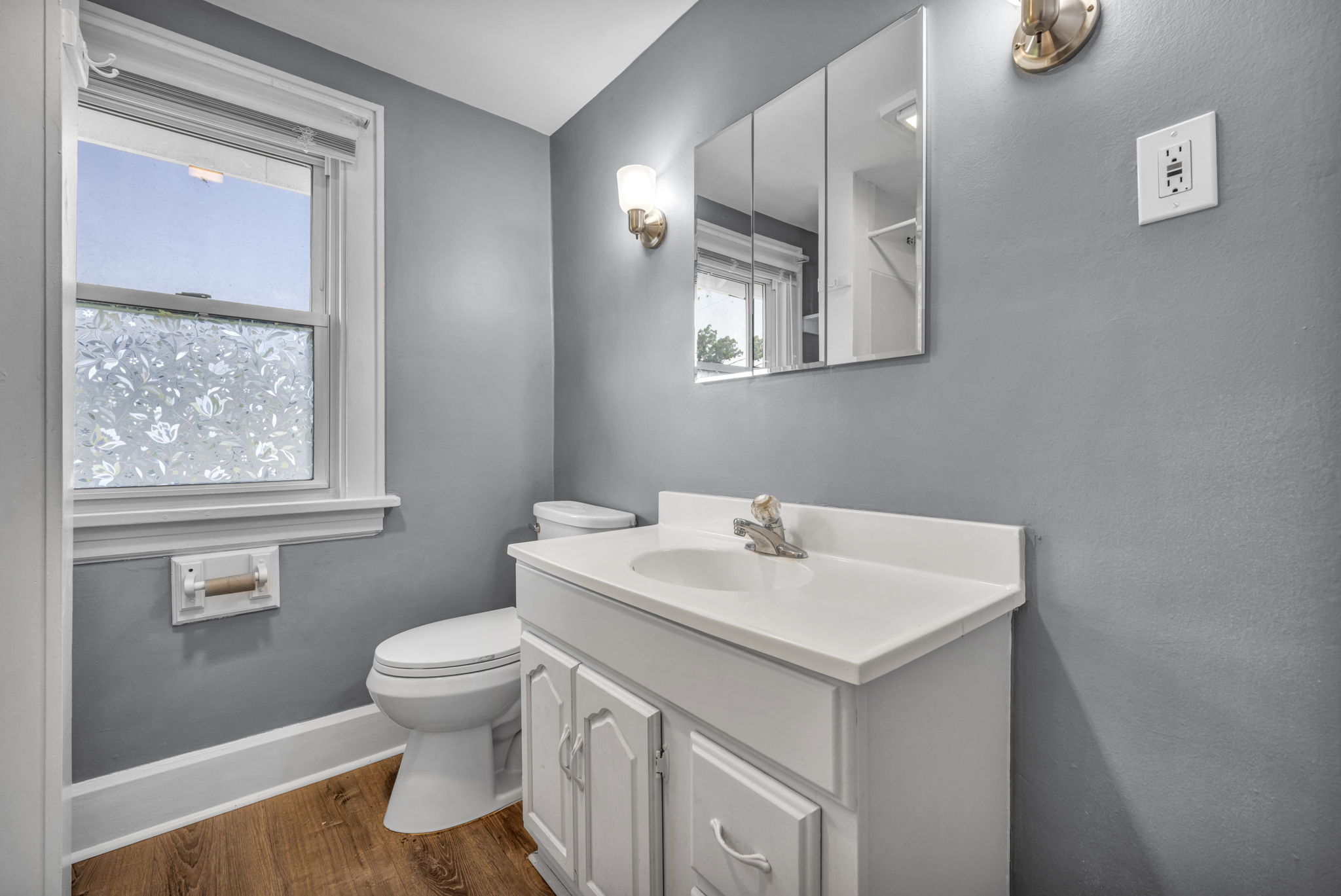bathroom showing vanity and toilet and window next to toilet with hardwood floors