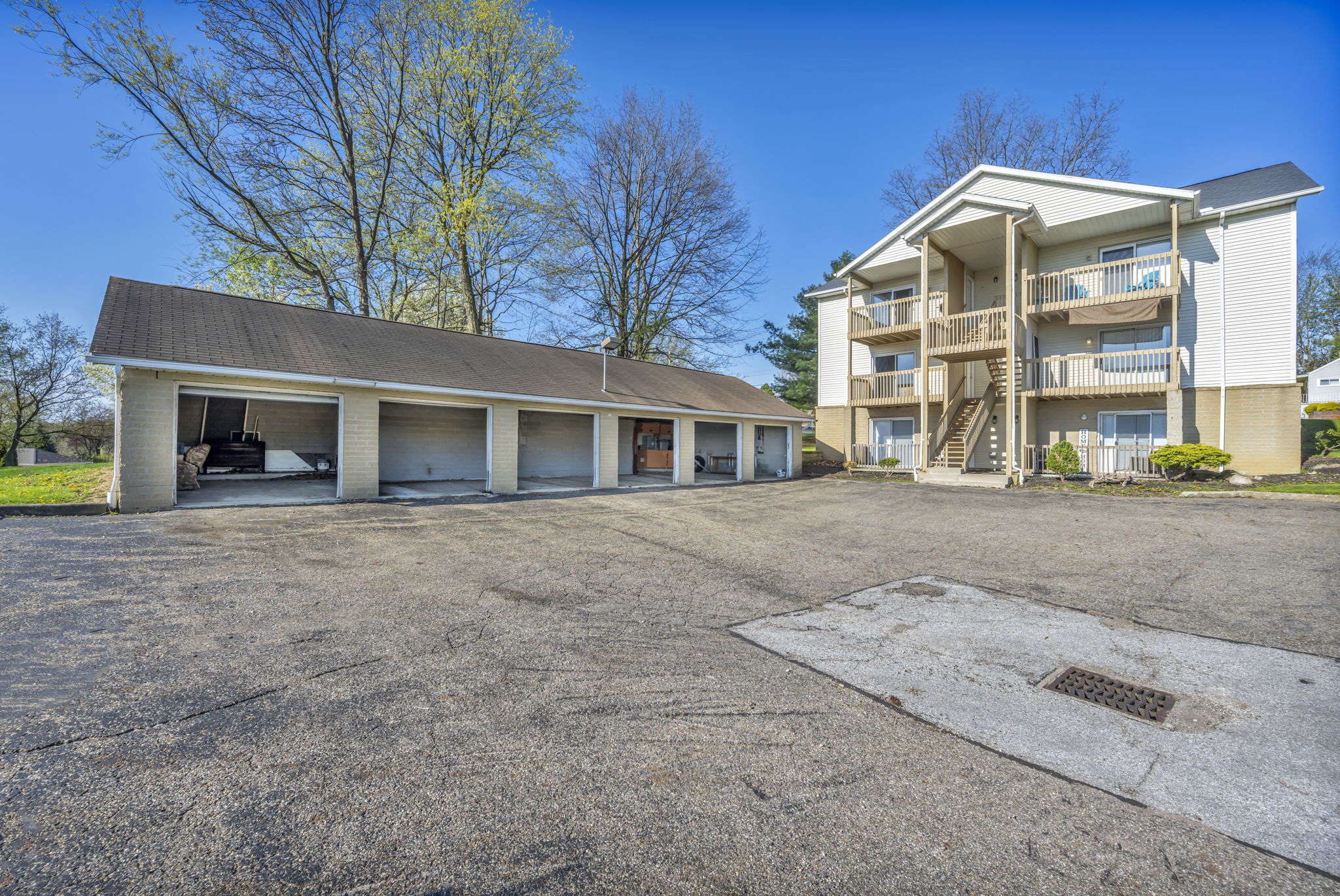 apartment exterior of 6 car garage with all doors open, rough pavement and 6 unit building in next to the garage