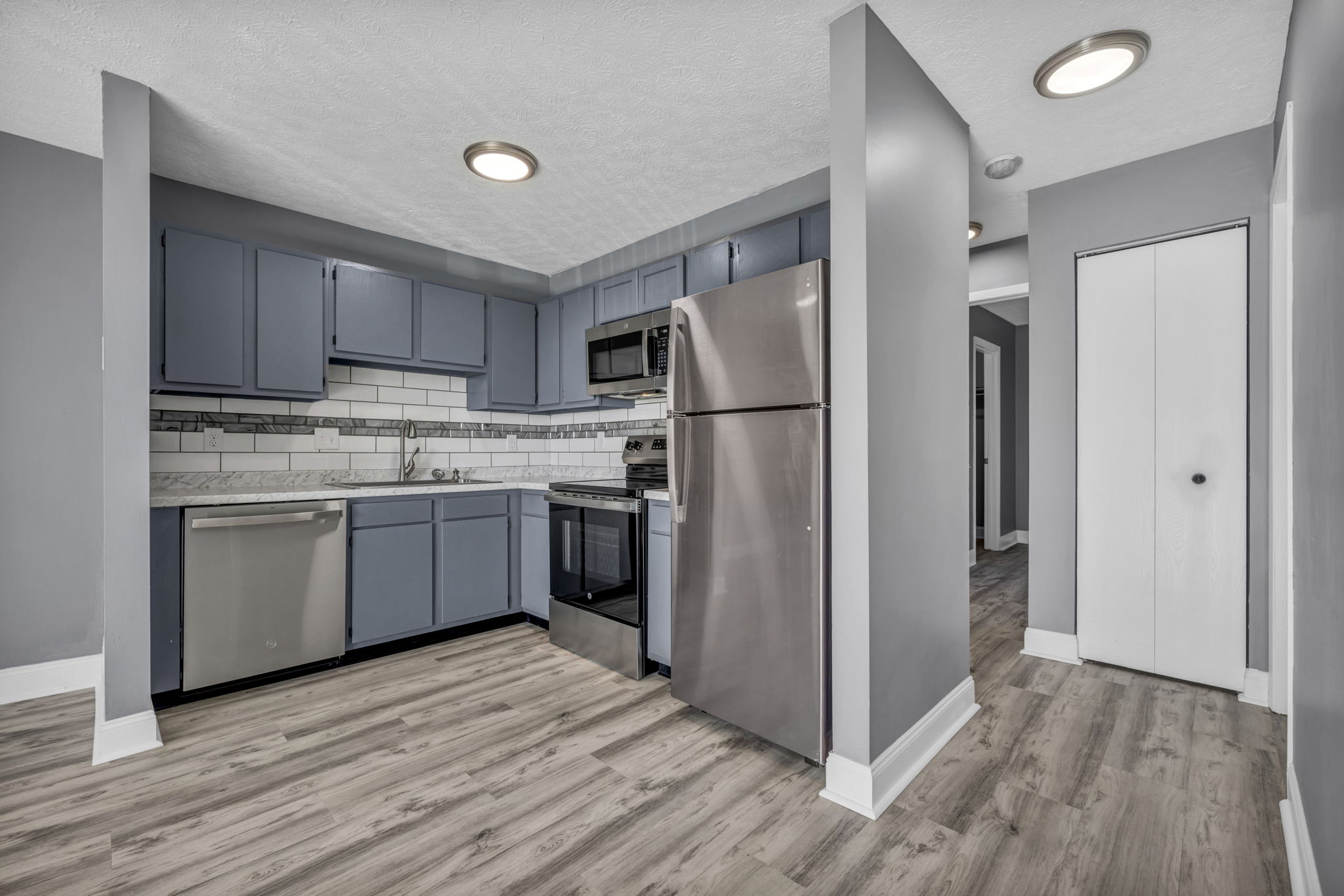 kitchen closeup of dark grey cabinets and stainless appliances with hallway to bedrooms