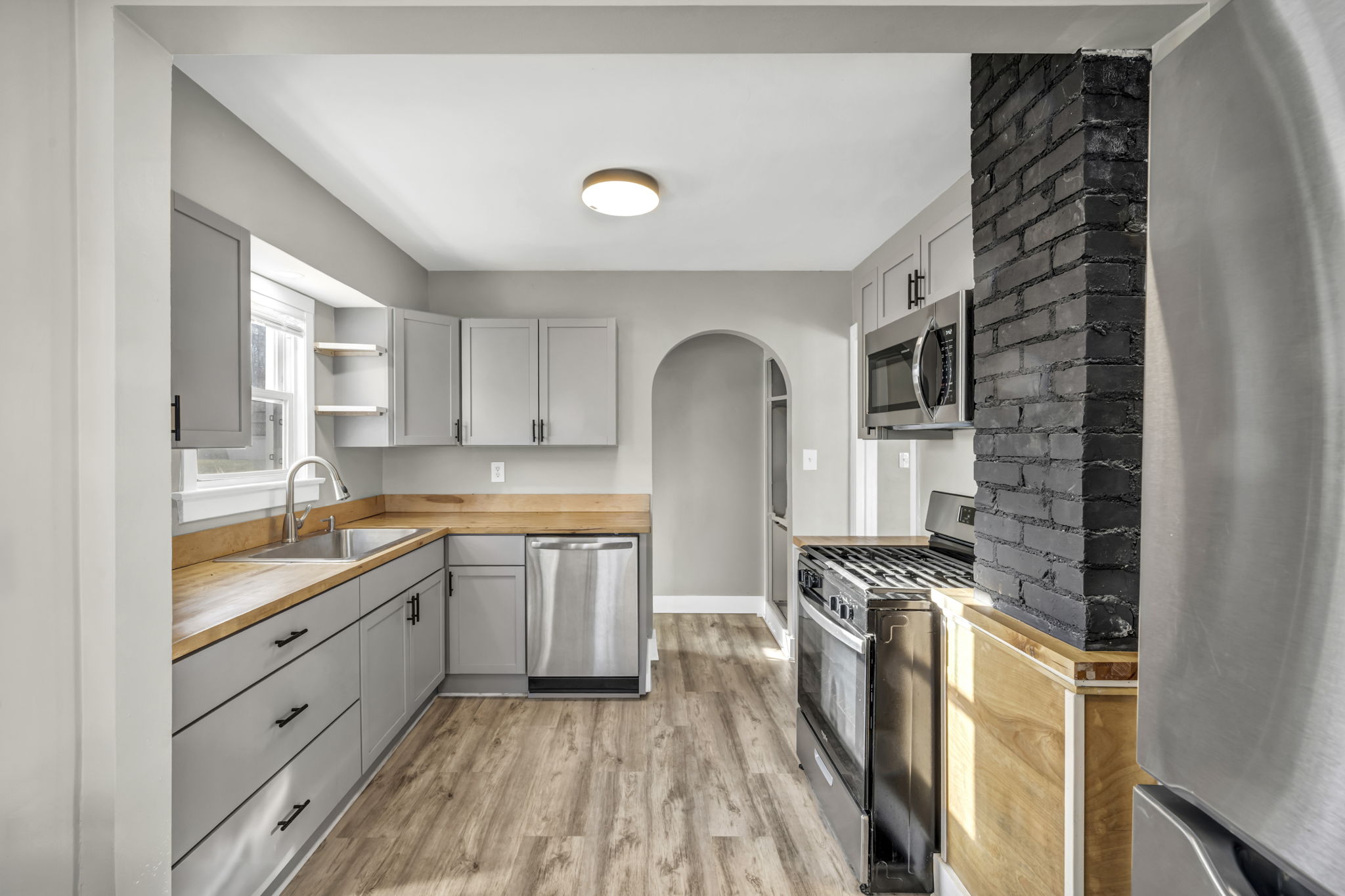 kitchen full view with grey cabinets, butcher block counter tops and close up of black painted brick