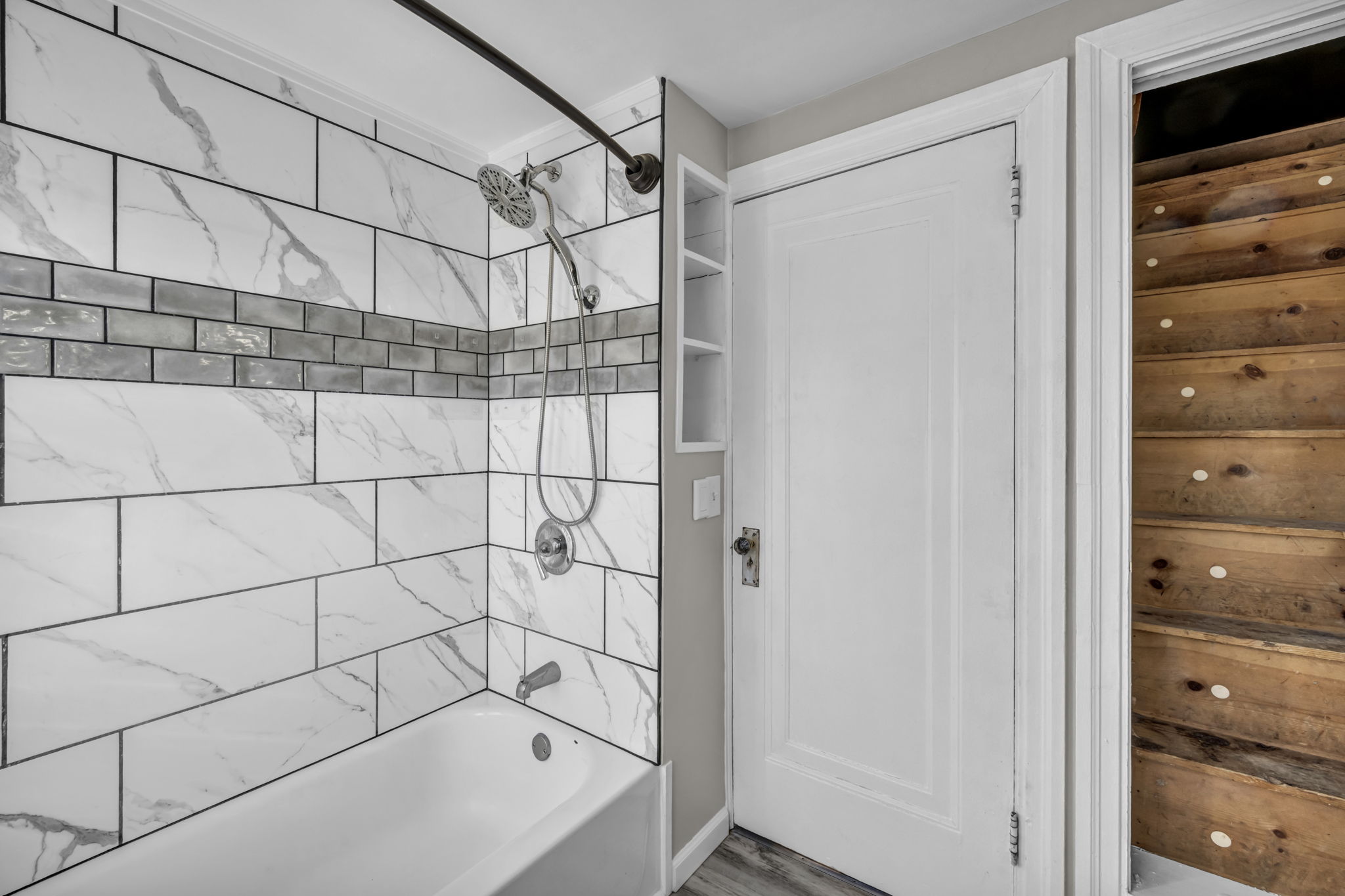 bathroom view of marble looking tile surrounding tub, a white door to exit, and the closet door open leading up into an attic