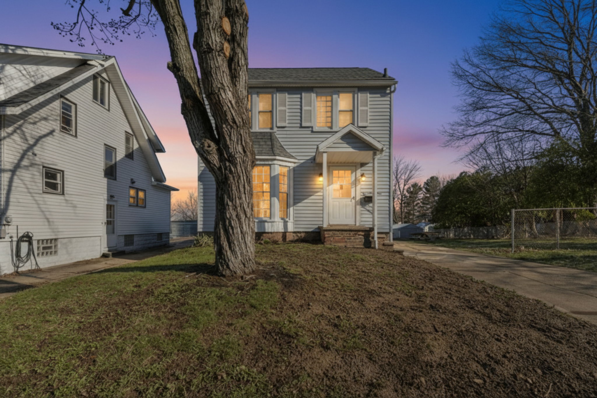 photo of colonial home at dusk with dirt yard and tree in the middle