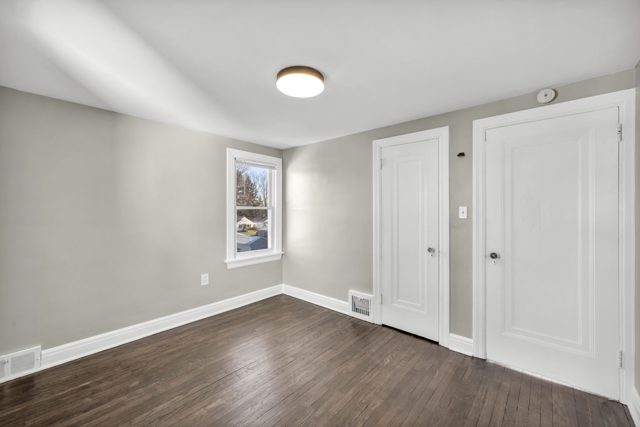bedroom with hardwood floors, white trim and two closet doors