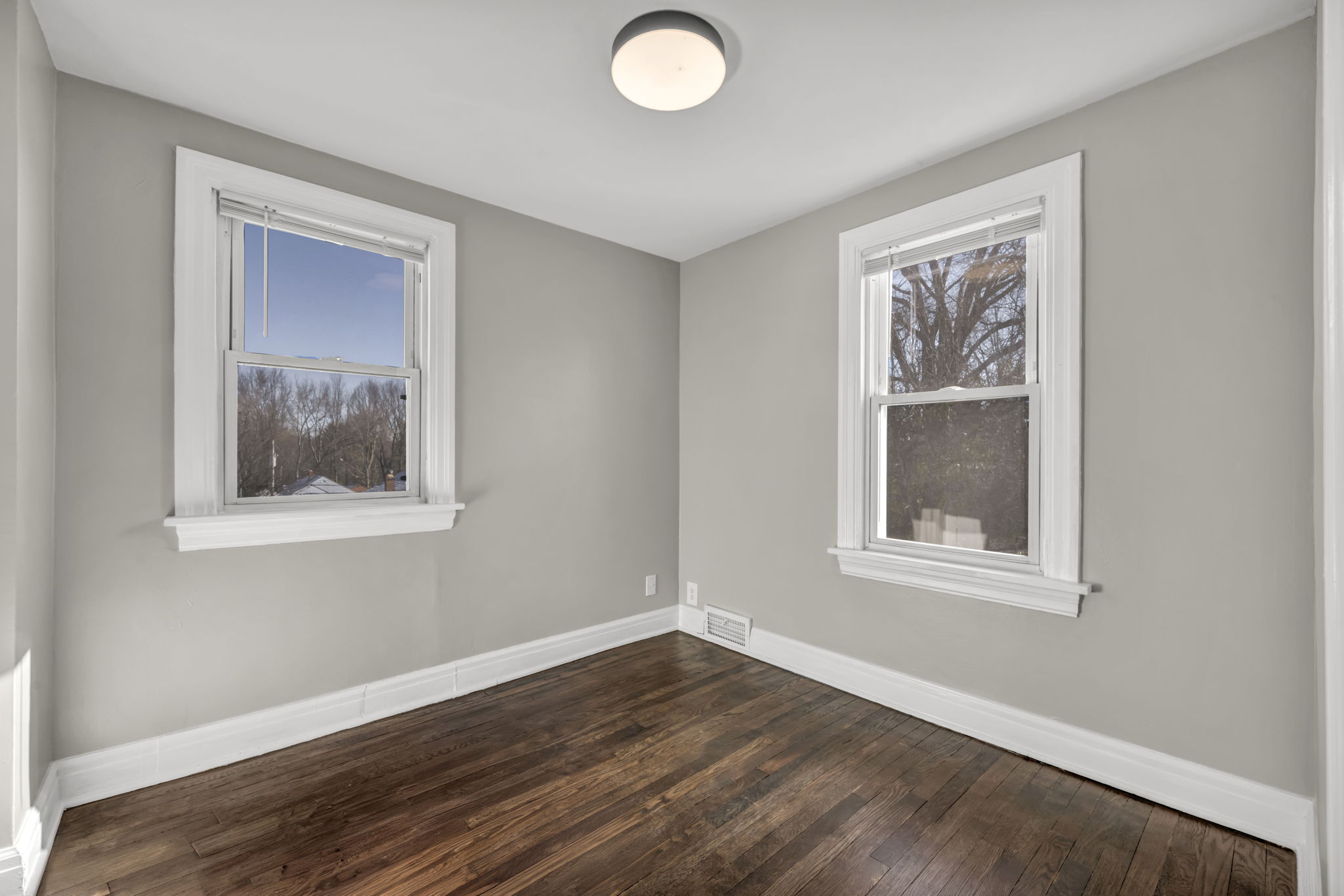 bedroom three with two windows, brown hardwood floors and a ceiling light